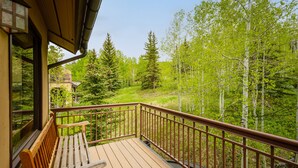 A wooden deck with a bench, a metal railing, and a view of a forested area. - Residence #31 3 Bedroom Home (Snowmass Village)