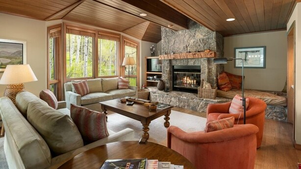 A cozy living room with a stone fireplace, wooden ceiling beams, and comfortable seating. - Residence #31 3 Bedroom Home (Snowmass Village)