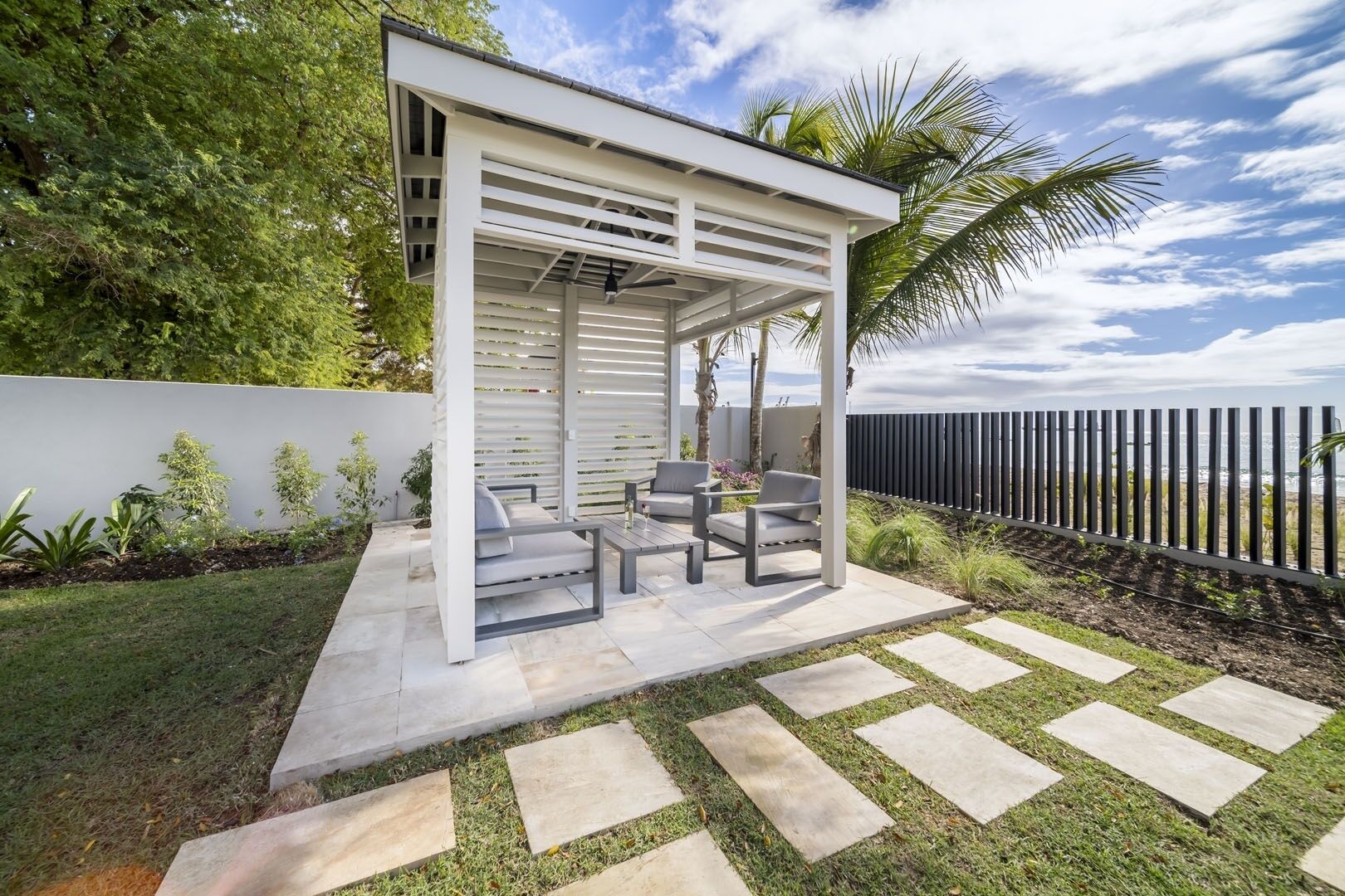 A covered outdoor seating area with a pergola, a stone pathway, and a view of the ocean.