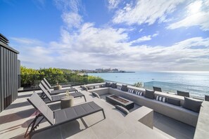 A rooftop terrace with a view of the sea, outdoor seating, and a glass balustrade.