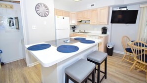 A modern kitchen with a central island, wooden cabinets, a built-in oven, and a flat-screen TV. - Coral Ridge 1 2 Bedroom Condo (Ocean City)