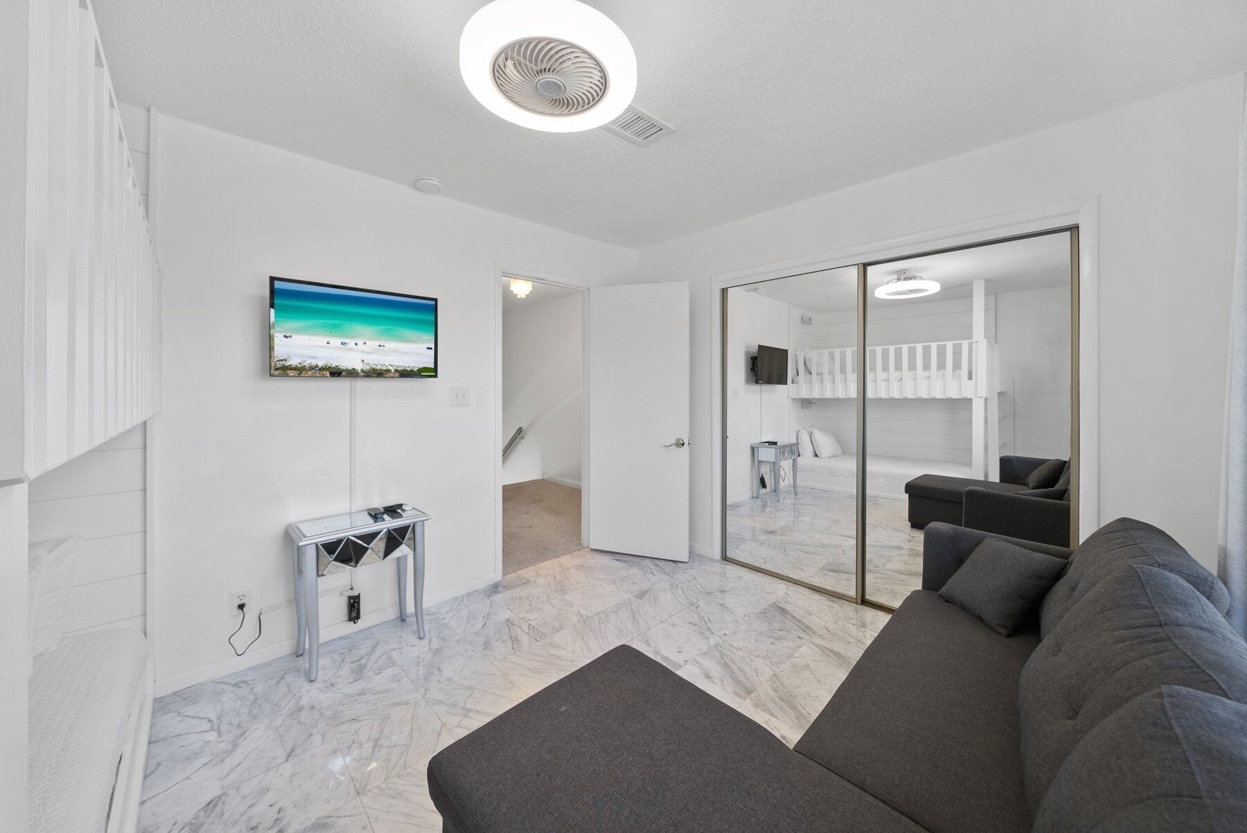 A modern living room with a grey sofa, a flat-screen TV mounted on the wall, and a small side table.