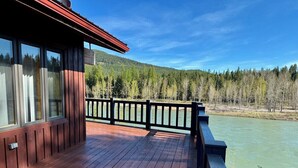 Una terraza de madera con barandilla, vista a un río y colinas boscosas.