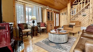 Un salón con piso de madera, una mesa redonda, dos sillones, un sofá y un mueble rojo.