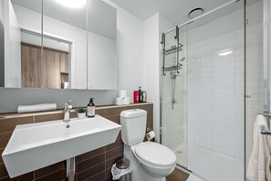 A modern bathroom with a white sink, toilet, and glass shower enclosure. - Stadium Spacious Corner Unit with Perfect Location (Melbourne)