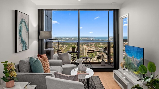A modern living room with a large window offering a city view, grey sofas, a coffee table, and a TV. - Sky Glow-Southbank Designer Glamour with Bay views (Southbank)
