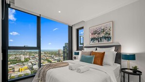 A modern hotel room with a large bed, a city view, a painting on the wall, and a small table with a lamp. - Sky Glow-Southbank Designer Glamour with Bay views (Southbank)