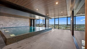 A modern indoor swimming pool with a city view, large windows, and a wooden ceiling. - Sky Glow-Southbank Designer Glamour with Bay views (Southbank)