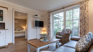 Ett mysigt vardagsrum med en soffa, ett träbord, en tv och ett fönster med gardiner.