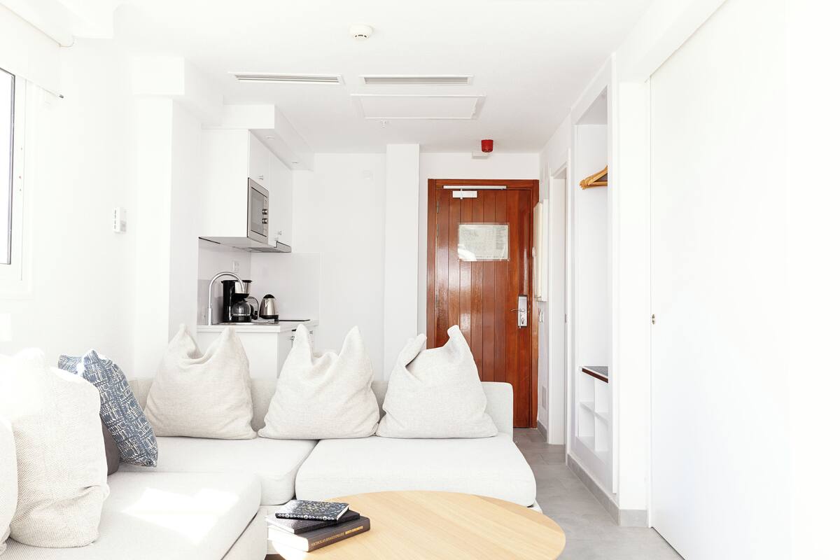 Un salon moderne avec un canapé blanc, une table basse et un coin cuisine à l’arrière-plan.