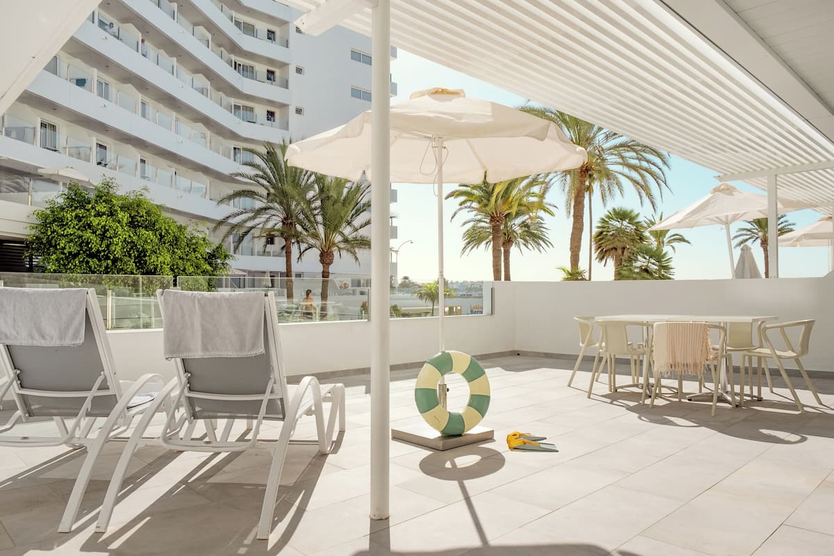 Une terrasse sur le toit, avec des chaises longues blanches, une table avec des chaises et des parasols.