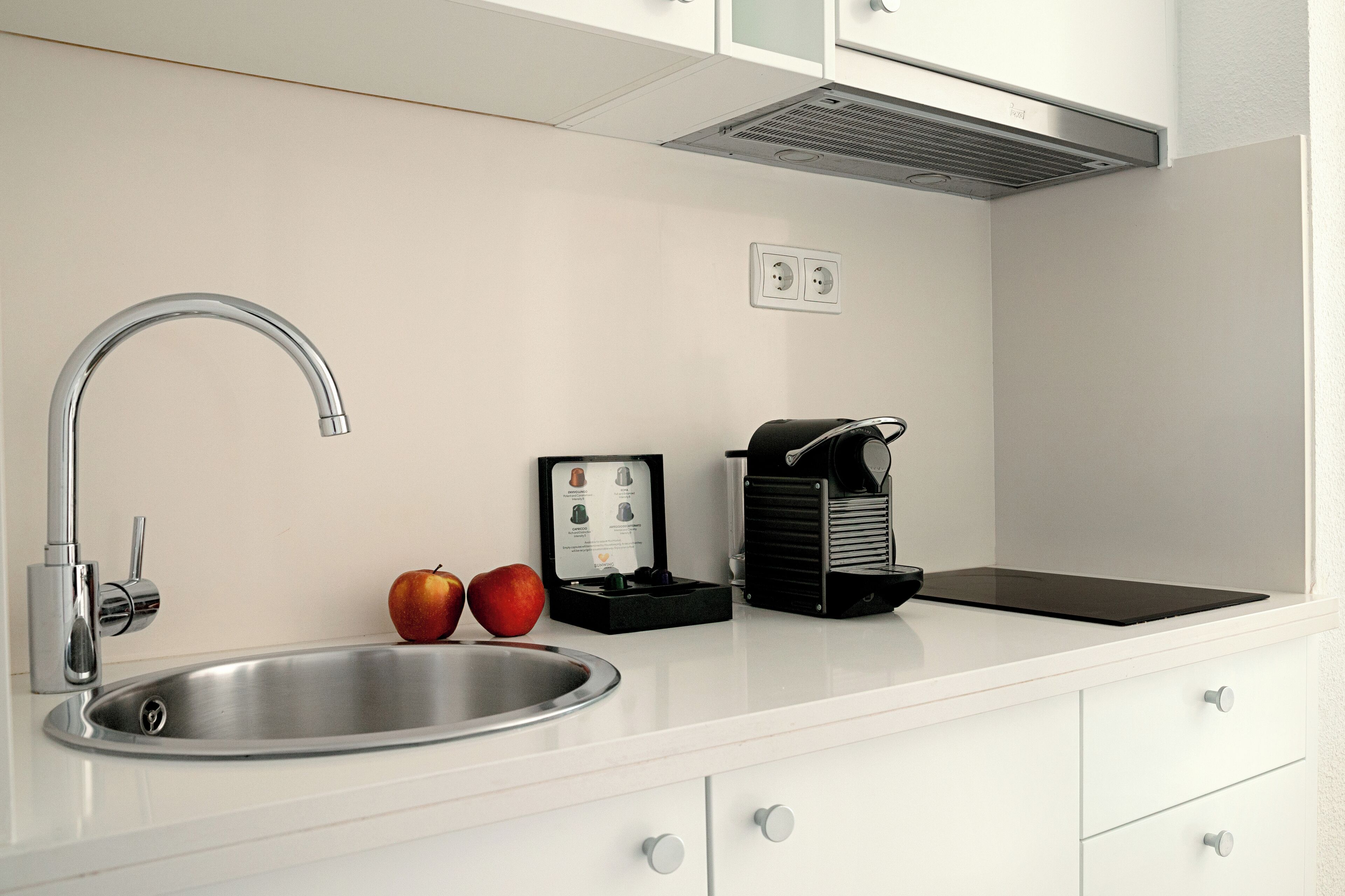 A modern kitchen with a stainless steel sink, a coffee maker, and two apples on the counter.