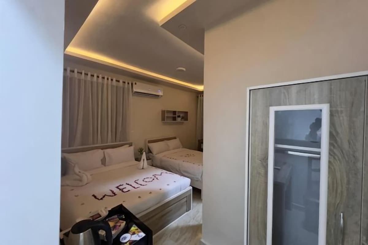 A modern hotel room with a bed, a wardrobe, a bedside table, and a window with curtains.