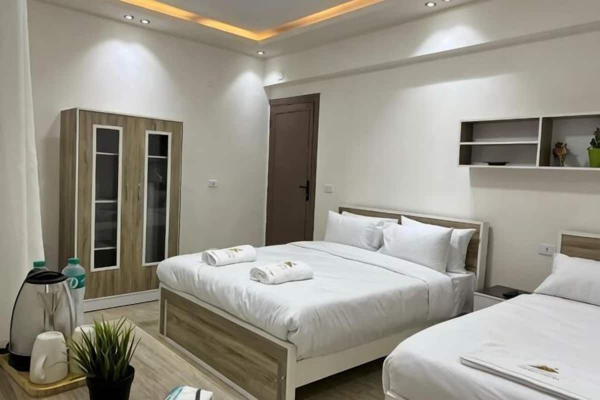 A modern hotel room with two beds, a wardrobe, a small desk, and a shelf with decorative items.