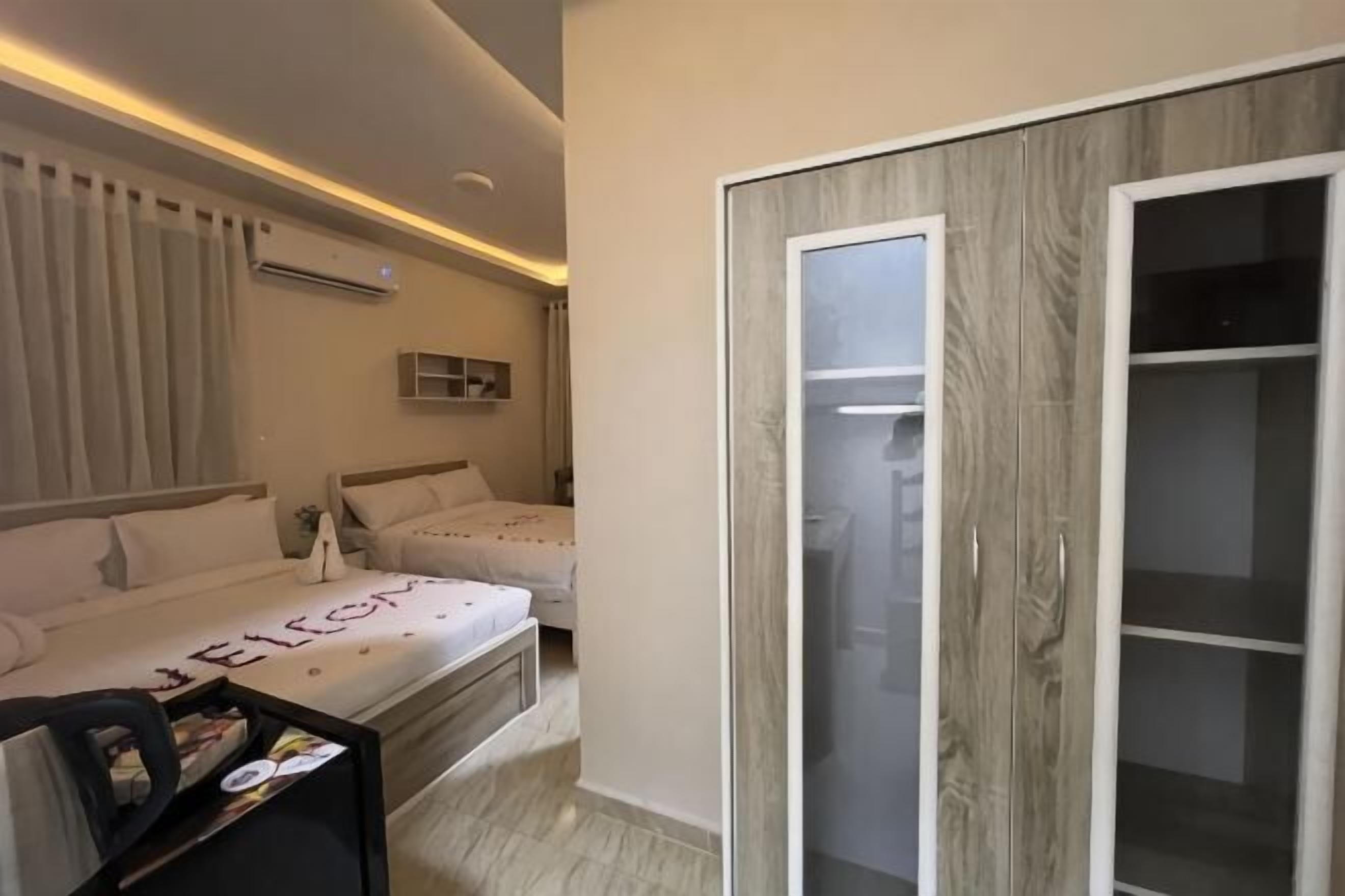 A hotel room with two beds, a wardrobe, a bedside table, and a mirror.