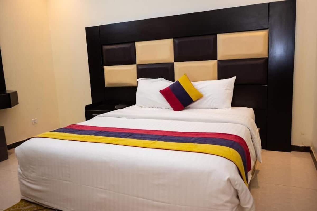 Una habitación de hotel con una cama grande, un cabecero estampado con cuadros y una manta decorativa de colores.