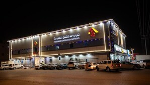 Ein Gebäude mit beleuchteter Beschilderung für Serviced Apartments, ein Parkplatz mit mehreren Autos und ein klarer Nachthimmel.