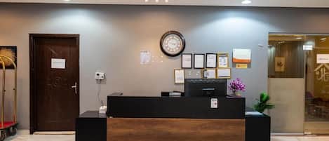 Un mostrador de recepción con un reloj, diplomas enmarcados y una planta pequeña.