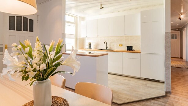 A modern kitchen with white cabinets, a wooden countertop, and a dining area with a vase of flowers. - Spacious Apartment in Strausberg - Sleeps 6 (Strausberg)