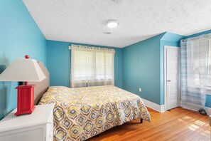 Une chambre à coucher avec un lit, une table de chevet avec une lampe, une fenêtre avec des rideaux et une porte.