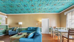 A living room with a teal patterned ceiling, a blue sofa, a wooden coffee table, and a dining area with chairs and a table.