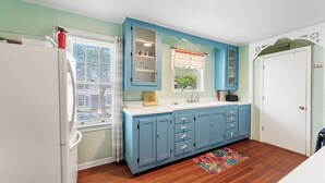 A kitchen with blue cabinets, a white refrigerator, a window with blinds, and a door with a no smoking sign.