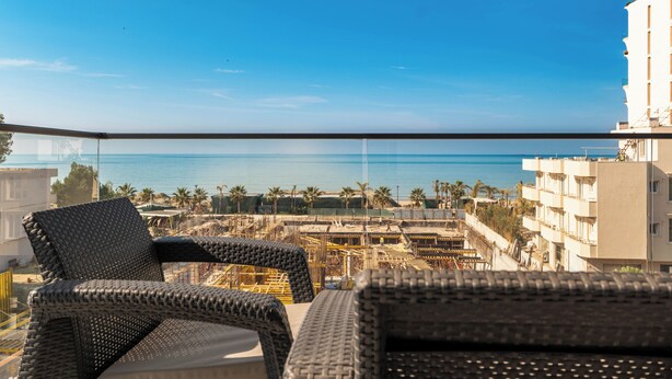 A balcony with wicker furniture overlooking a construction site and the sea. - Golemi Lux Hotel (Golem)