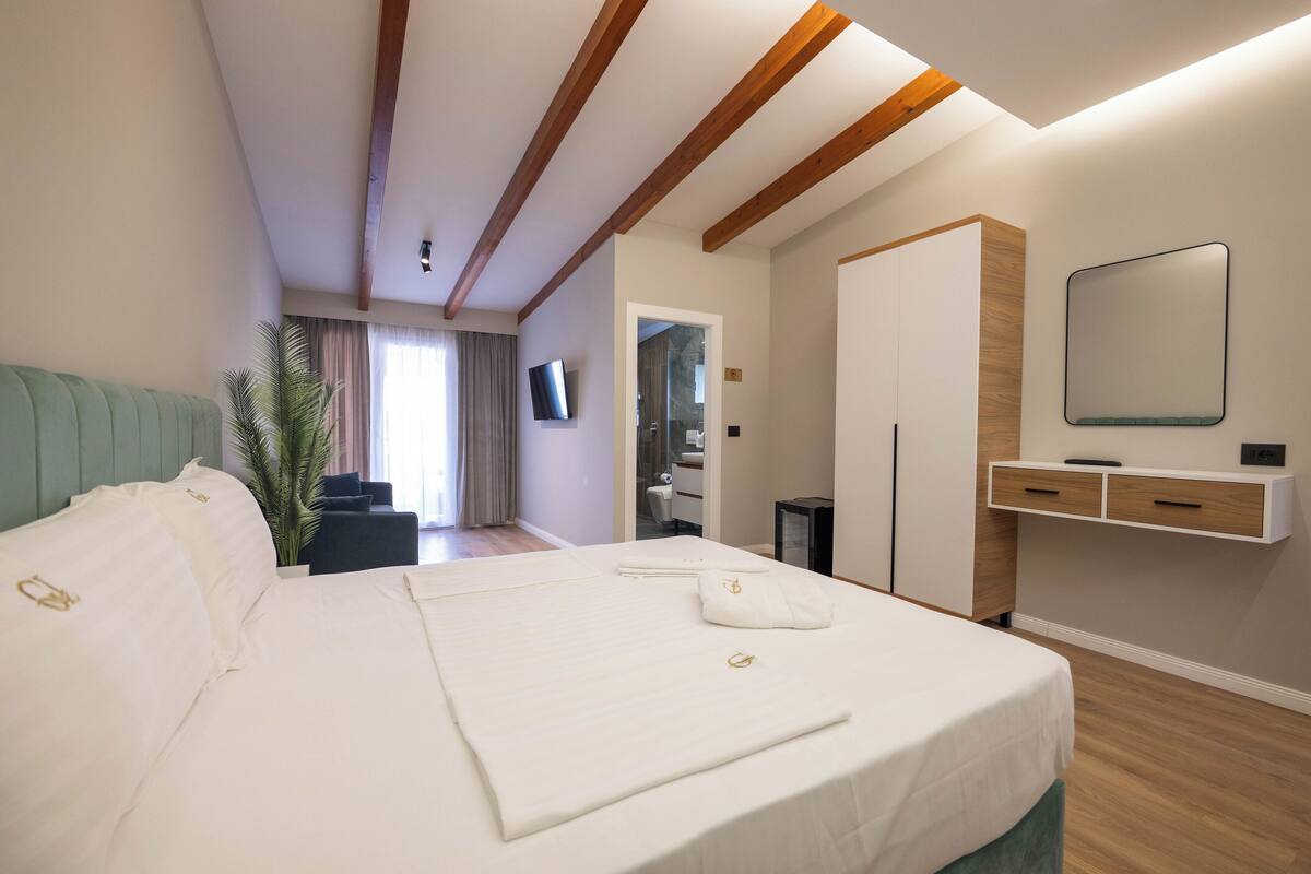 A hotel room with a large bed, a desk, a mirror, and a television.