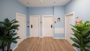 A hallway with light blue walls, wooden flooring, and white doors. There are two potted plants, one on each side of the hallway. - Golemi Lux Hotel (Golem)