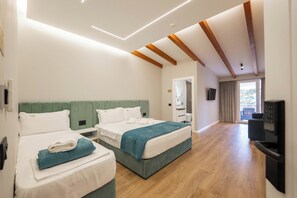 Ein Hotelzimmer mit zwei Betten, Holzboden, Fernseher und einem Fenster mit Vorhängen.