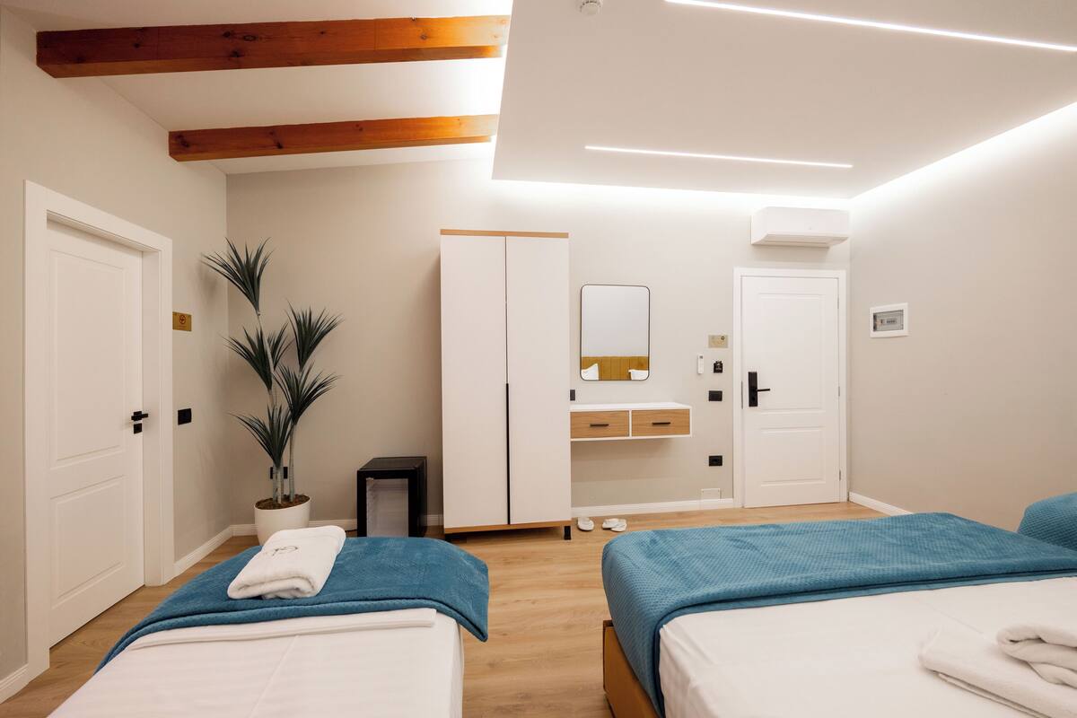 A hotel room with two beds, a wardrobe, a mirror, a potted plant, and a small table.
