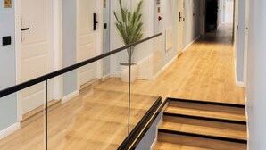 A hotel corridor with wooden flooring, white doors, a glass railing, and a potted plant. - Golemi Lux Hotel (Golem)