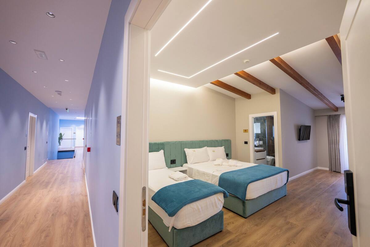A hotel room with two beds, a bathroom, and a hallway.