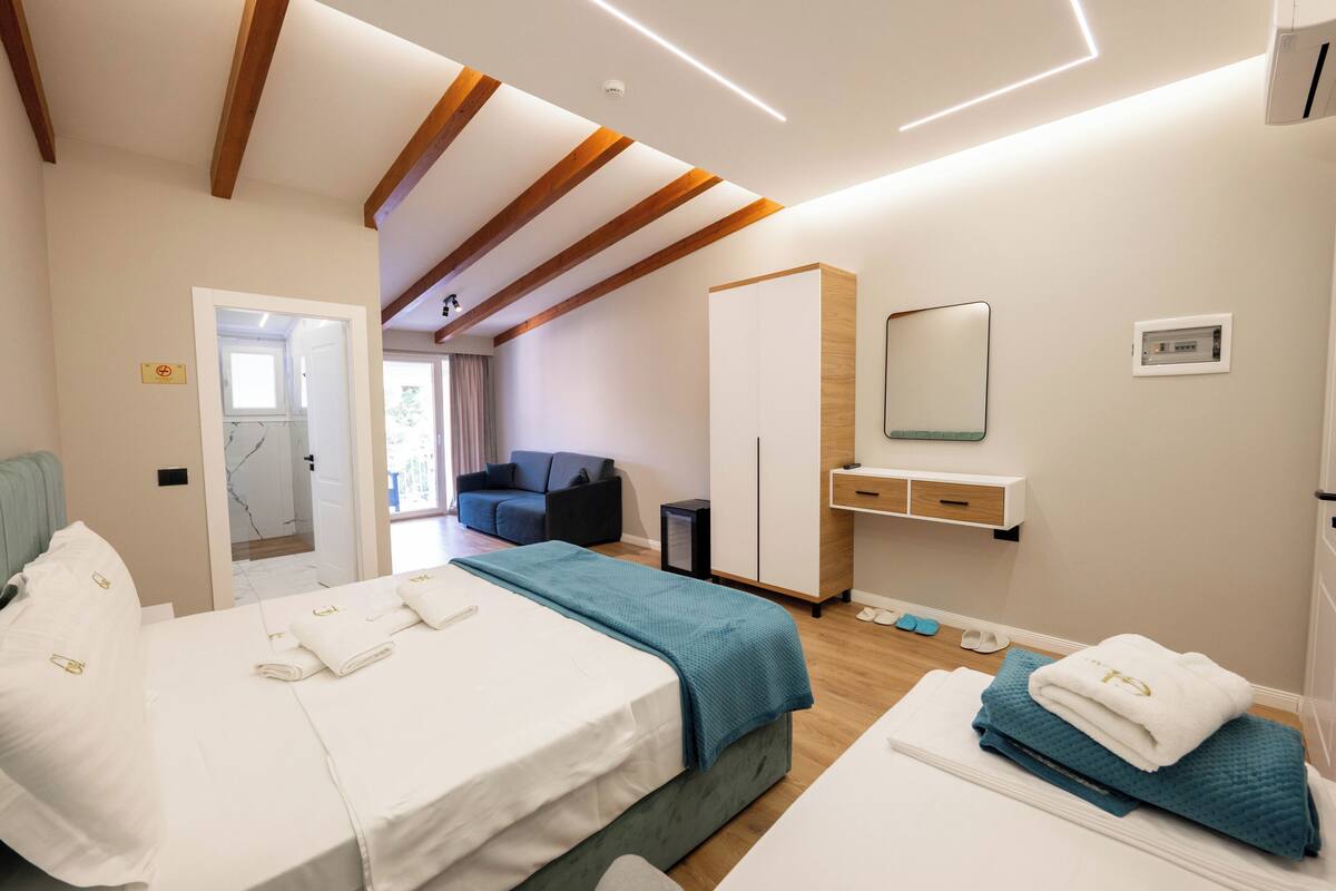 A modern hotel room with a large bed, a desk, a wardrobe, and a bathroom visible through an open door.