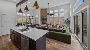 A spacious kitchen with a large island, modern pendant lighting, and a stone fireplace.
