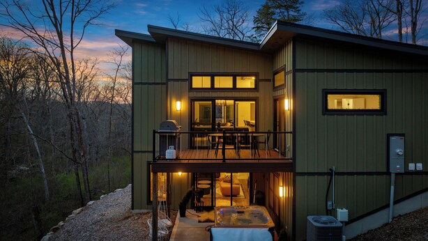 A modern two-story house with a balcony, a hot tub, and a patio area.