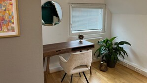 Opiskeluhuone, jossa on puinen työpöytä, valkoinen tuoli, maapallo, ruukussa oleva kasvi ja ikkuna, jossa on sälekaihtimet.