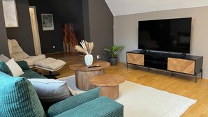 Moderni olohuone, jossa on kulmasohva, sohvapöytä, TV-taso ja suuri, litteänäyttöinen televisio.