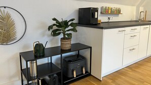 Moderni keittiö, jossa on musta työtaso, valkoiset kaapit, kahvinkeitin, vedenkeitin ja ruukkukasvi.