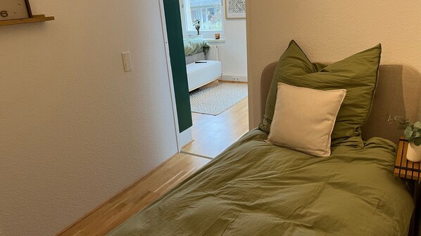 A narrow hallway leading to a bedroom with a bed, pillows, and a nightstand with a plant.