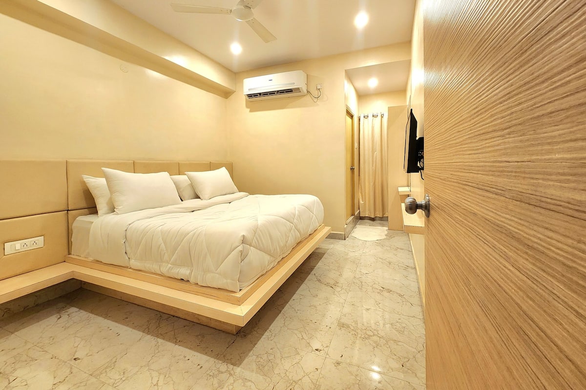 A modern bedroom with a bed, ceiling fan, air conditioning unit, and a wooden door.