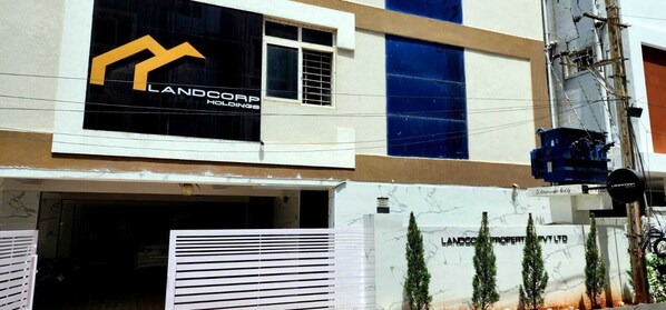 Um edifício com uma placa grande da LANDCORP Holdings, entrada com portão e vista desobstruída da região ao redor.