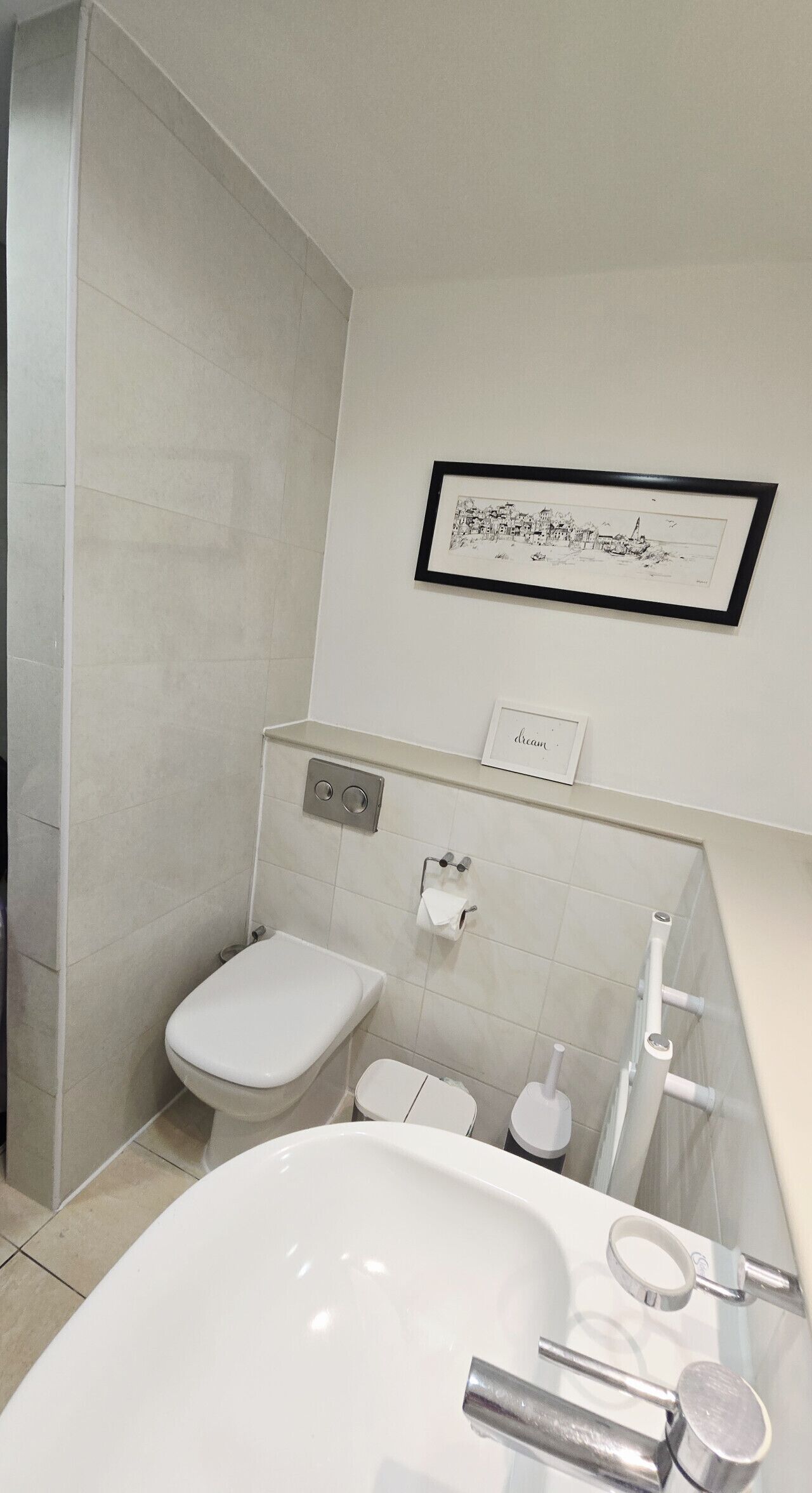 Een moderne badkamer met een bad, toilet en bidet. Aan de muur hangt een lijst met een foto en een bordje met de tekst 'dream'.