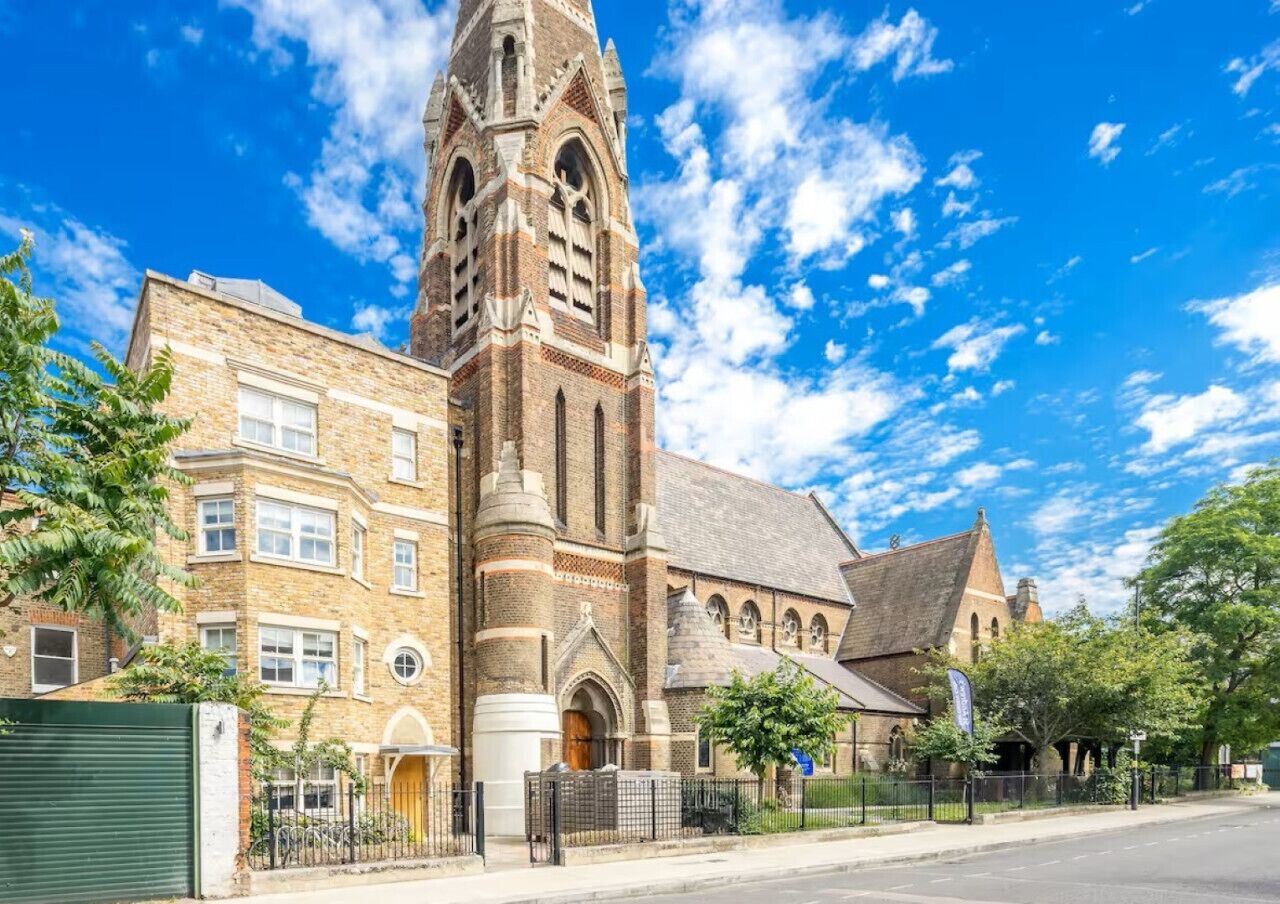 Een historisch kerkgebouw met een opvallende toren, aangrenzende woongebouwen en een heldere blauwe lucht.