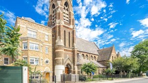 Une église historique dotée d’un clocher imposant, des immeubles résidentiels adjacents et un ciel d’un bleu éclatant.