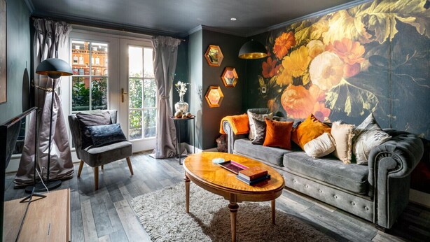 Un salon moderne avec un canapé gris, une table basse en bois et une grande fresque florale sur le mur.