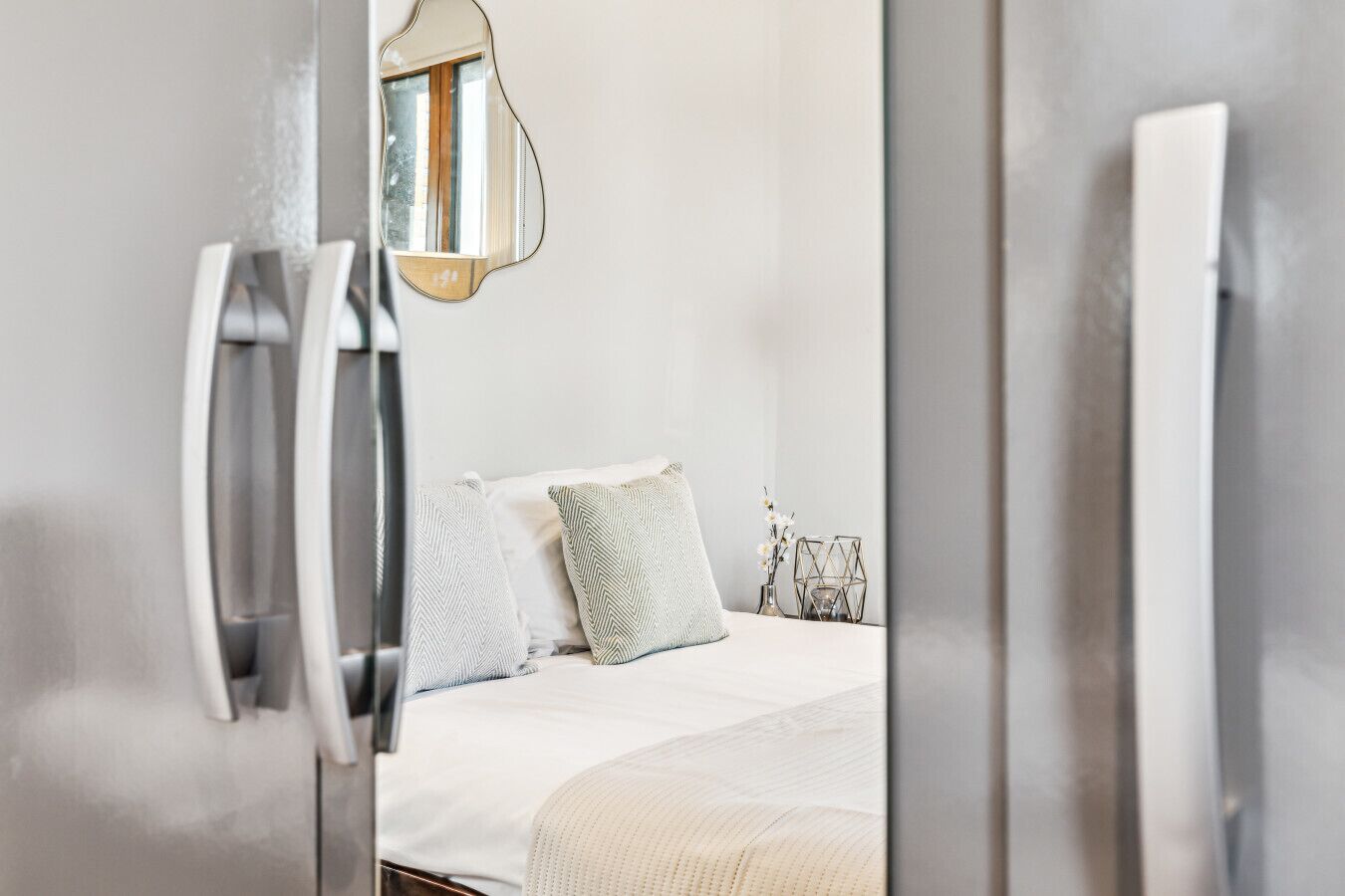 A modern hotel room with a bed, a mirror, and a bedside table.