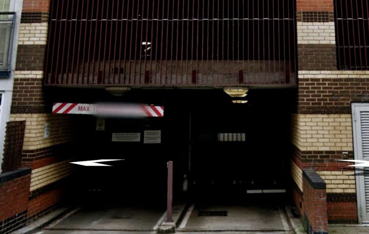A building entrance with a metal gate, a red and white striped sign, and a brick facade.