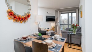 A modern living room with a dining area, a flat-screen TV, and a large window with curtains. - Lovely 3BD Flat, Parking, sleeps SIX close to O2 (London)