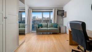 A modern apartment with a wooden floor, a green sofa with teal cushions, a black office chair, and a small desk. - Lovely 3BD Flat, Parking, sleeps SIX close to O2 (London)
